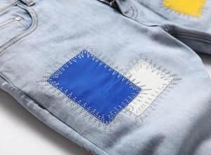 Macro detail of men's slim fit jeans with colorful patchwork and contrast white stitching