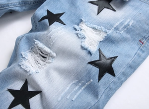 Close-up of distressed light blue denim shorts with black leather star patches and ripped details