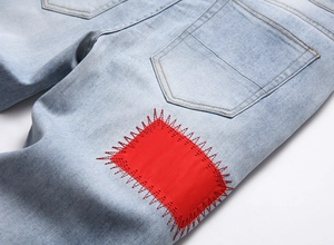 Close-up of light blue washed denim jeans featuring a bold red square patch with red stitching