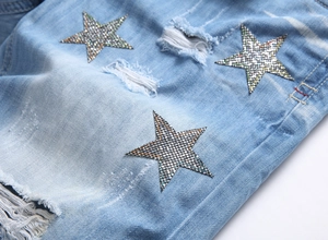 Detail of light blue denim shorts featuring rhinestone star patches and ripped effects