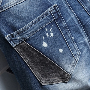 Men's blue distressed denim shorts with unique black patchwork and white paint splatters
