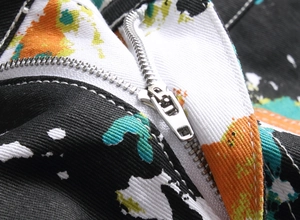 Macro shot of a silver metal zipper on street style jeans with colorful paint splatters
