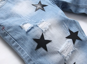 Detailed macro view of light blue denim shorts featuring black leather star patches and rips