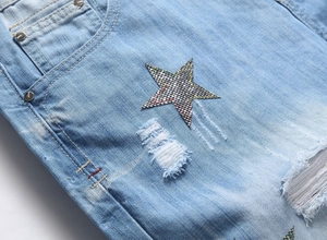 Detail of star embroidery with distressed rip and denim texture on men's blue shorts
