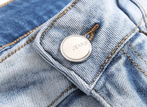 Macro shot of silver metal button with JEANS engraving and yellow stitching on blue denim