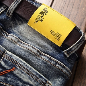 Detail of dark blue denim jeans with a yellow leather label and a brown belt on wood
