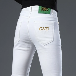 Detailed close-up of gold CNC embroidery and green leather logo patch on white denim jeans