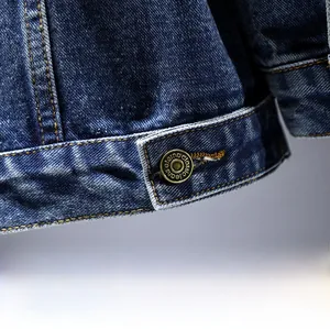 Close-up of vintage brass button on dark blue denim jacket with yellow stitching