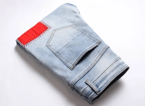 Close-up of a light blue washed denim jeans featuring a unique red patch with zigzag stitching
