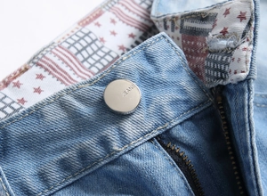 Detailed macro view of light blue denim jeans with silver metal button and star inner lining