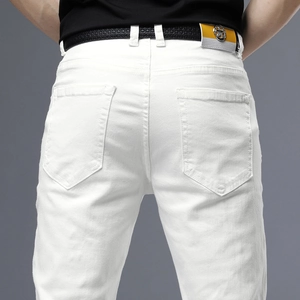 Détail d'un jean blanc ajusté avec ceinture en cuir noir et étiquette jaune avec étoile