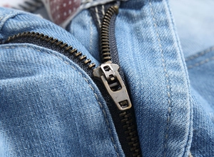 Detailed close-up of a bronze metal zipper on light blue denim shorts with stitching