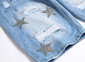 Macro shot of light blue washed denim with ripped distressed details and star rhinestone patch