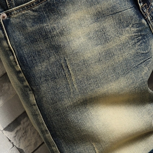 Close-up of vintage blue denim fabric with yellow washed texture and metal rivet detail