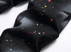 Detail of black slim denim jeans featuring colorful paint splatter and grey washed texture