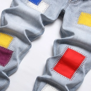 Men's slim fit light blue denim jeans featuring colorful geometric patches and hand-stitched detail