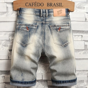 Gros plan du short en jean bleu clair avec coutures orange et écusson de marque en cuir