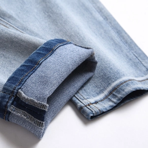 Slim fit light blue distressed denim jeans showing rolled cuffs and stitching detail