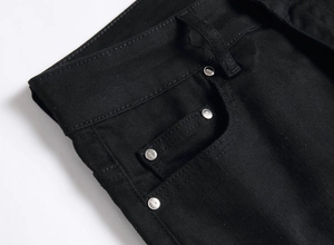 Detail of black denim jeans featuring metal rivets and textured waistband construction