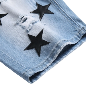 Light blue washed denim shorts with distressed ripped holes and black star patchwork detail