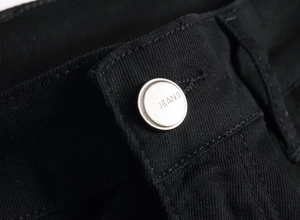Close-up of a silver metal button with JEANS engraving on black denim fabric