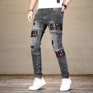Détail du jean skinny gris usé avec écussons lettrés colorés et effets déchirés