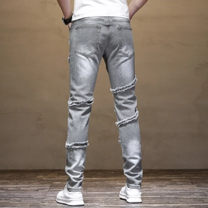 Detail of light grey slim-fit men's jeans with distressed horizontal frayed knee slits