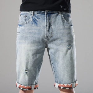 Detail of light blue denim shorts featuring ethnic embroidery trim and distressed hole design