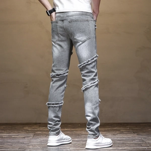 Detail view of light grey denim jeans with heavy distressed rip design on back of legs