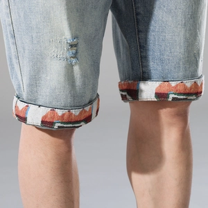 Detail of light blue denim shorts with distressed holes and colorful patterned cuffs