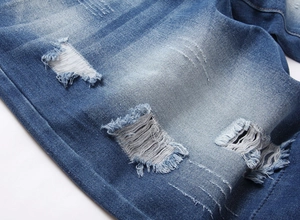 Close-up of distressed denim fabric with ripped hole detail and white thread texture
