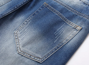 Close-up of distressed denim back pocket featuring stone-washed blue and rip details