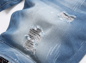Detailed close-up of light blue distressed denim fabric with ripped holes and star pattern