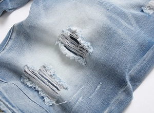 Detailed close-up of heavy distressed ripped texture on light blue denim shorts