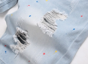 Detail of light blue denim shorts with distressed ripped holes and colorful paint splatter