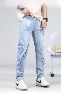 Détail d'un jean bleu clair avec des déchirures et des sangles à boucles métalliques