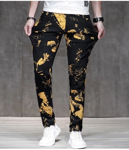 Macro detail of men's slim fit black denim jeans featuring golden graffiti ink splatter print