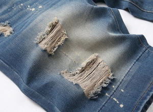 Detailed close-up of distressed denim shorts with ripped holes and white paint splatters