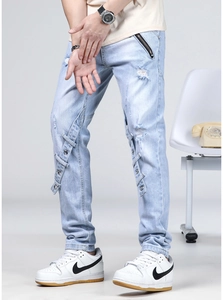 Détail du jean slim bleu clair avec des trous vieillis et des sangles à crochet en métal