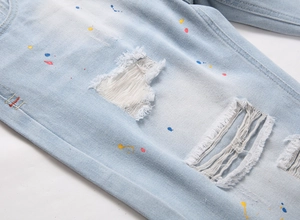 Detailed close-up of light blue distressed denim shorts with paint splatters and frayed holes