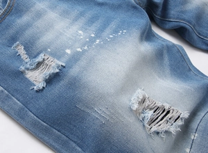 Detailed close-up of blue washed denim shorts with distressed rips and white paint splatters