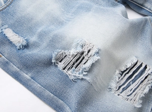 Detail of light blue washed denim shorts featuring ripped holes and distressed fringe texture