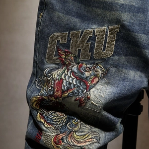 Detailed close-up of intricate koi fish embroidery and gold CKU lettering on blue denim shorts