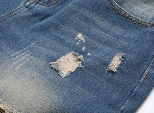 Detail view of denim shorts featuring heavy distressing, frayed holes, and white paint splatters