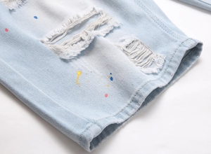 Detail of light blue denim shorts featuring distressed rips and colorful paint splatter accents