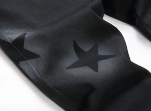 Detail of black fabric featuring matte star patterns and twill texture on denim pants