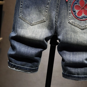 Detailed embroidery of red flowers and round patterns on dark blue denim shorts pocket