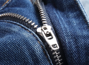 Macro close-up of silver metal zipper and stitching on dark blue denim shorts