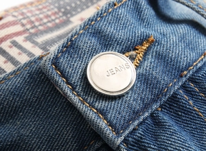 Gros plan sur un denim bleu épais avec coutures orange et bouton en métal argenté