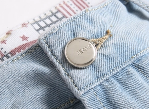 Detailed close-up of a silver jeans button on light blue denim shorts with star pattern lining